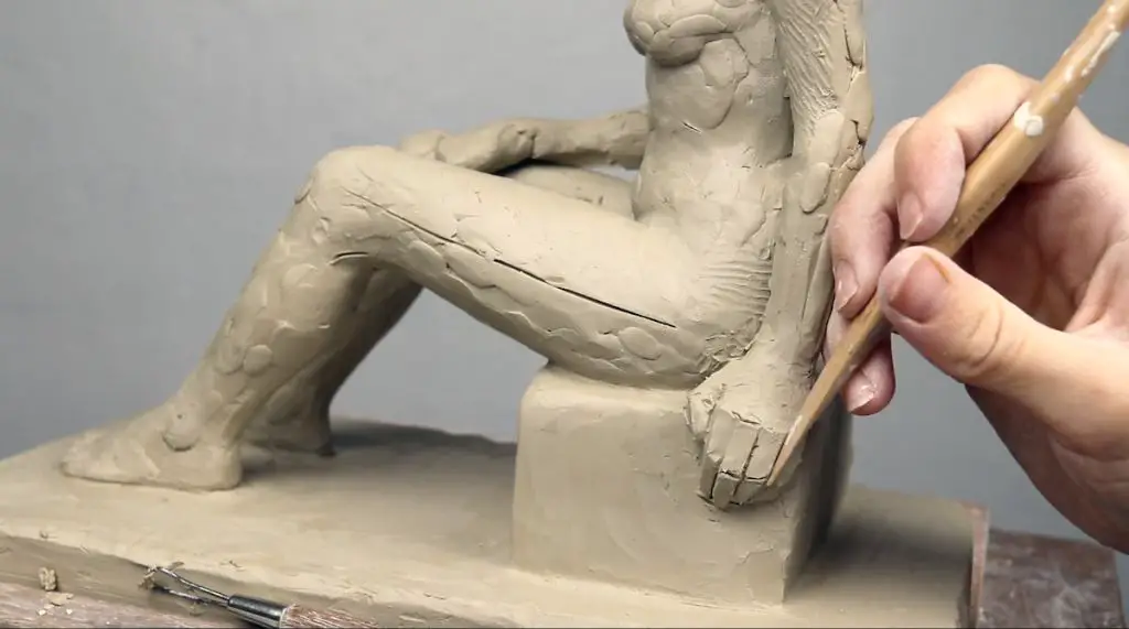 a beginner clay sculptor working with clay sculpting tools on a human figure sculpture