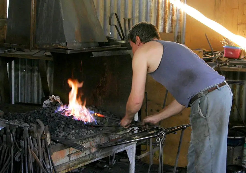 a blacksmith removing a red hot steel part from a forge and quenching it in a bucket of water to harden it