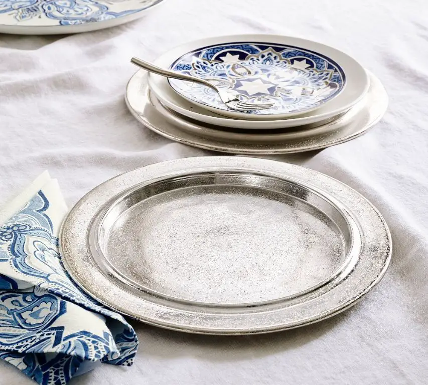 a charger plate made from silver metal underneath a porcelain dinner plate