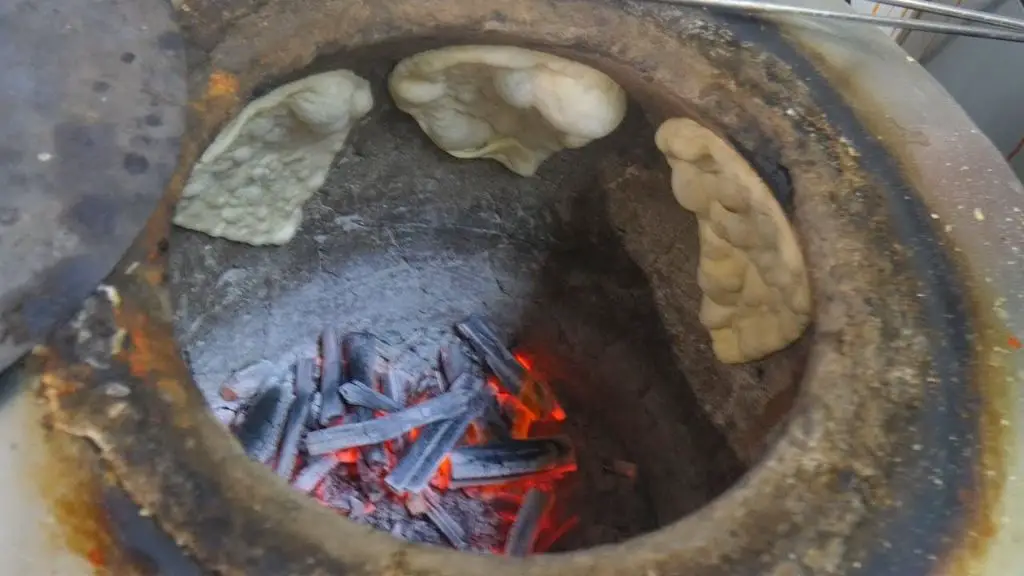 a chef preparing naan bread in a traditional indian tandoor oven.