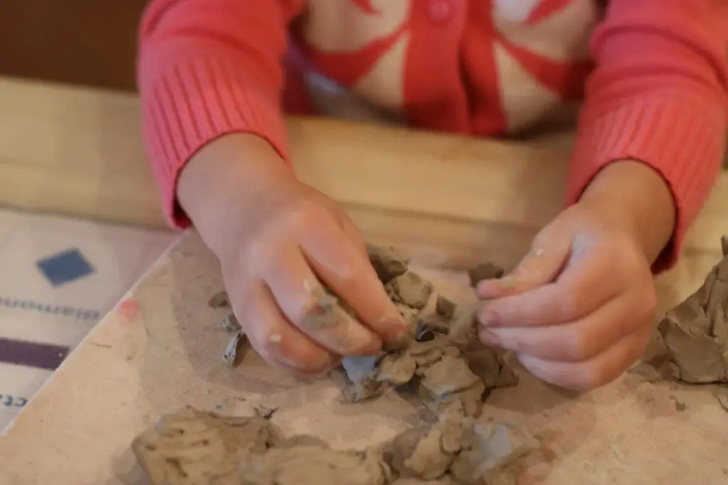 a child playing with modeling clay, pounding it with their fist to explore the auditory sensory qualities