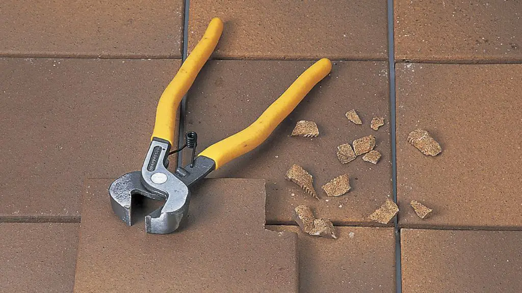 a close up image of tile nippers being used on a tile edge