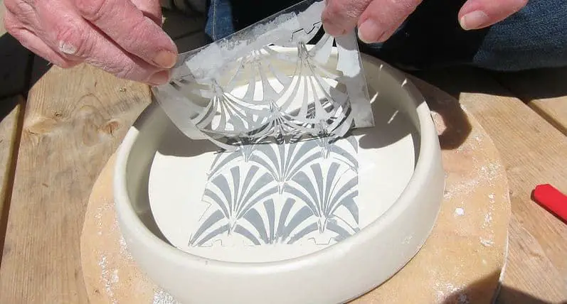 a container of white commercial underglaze being brushed onto a piece of pottery