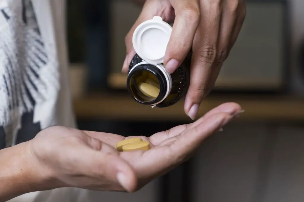 a hand holding a bottle of tricalcium phosphate supplements, which can potentially cause side effects if taken in excess.