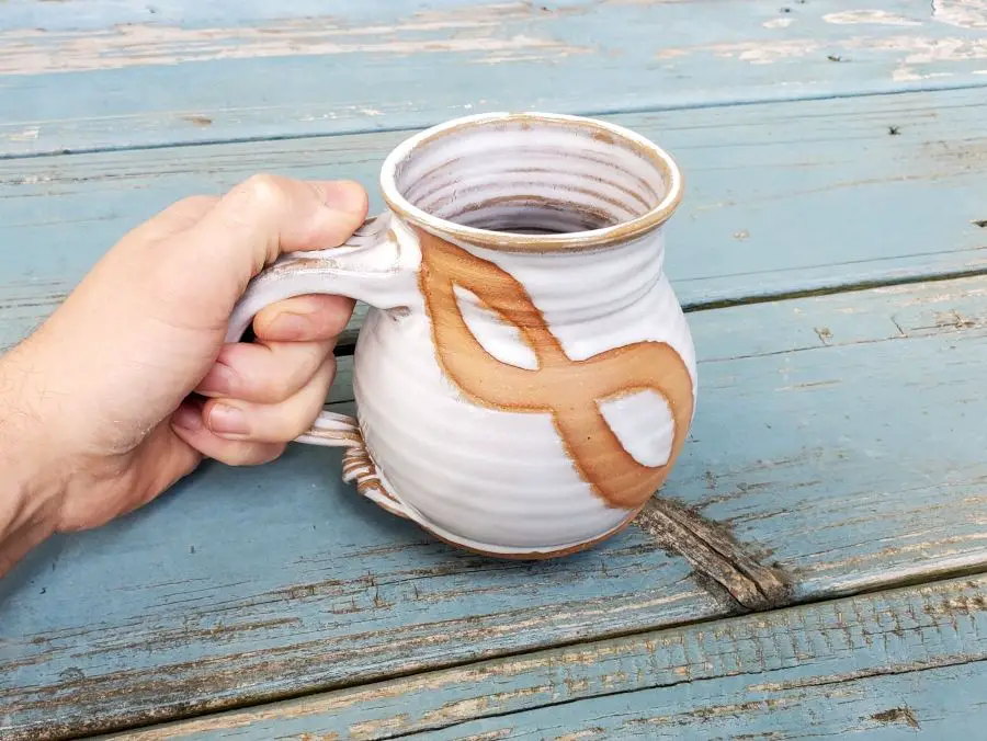 a hand holding a handmade ceramic coffee mug with a unique glaze design