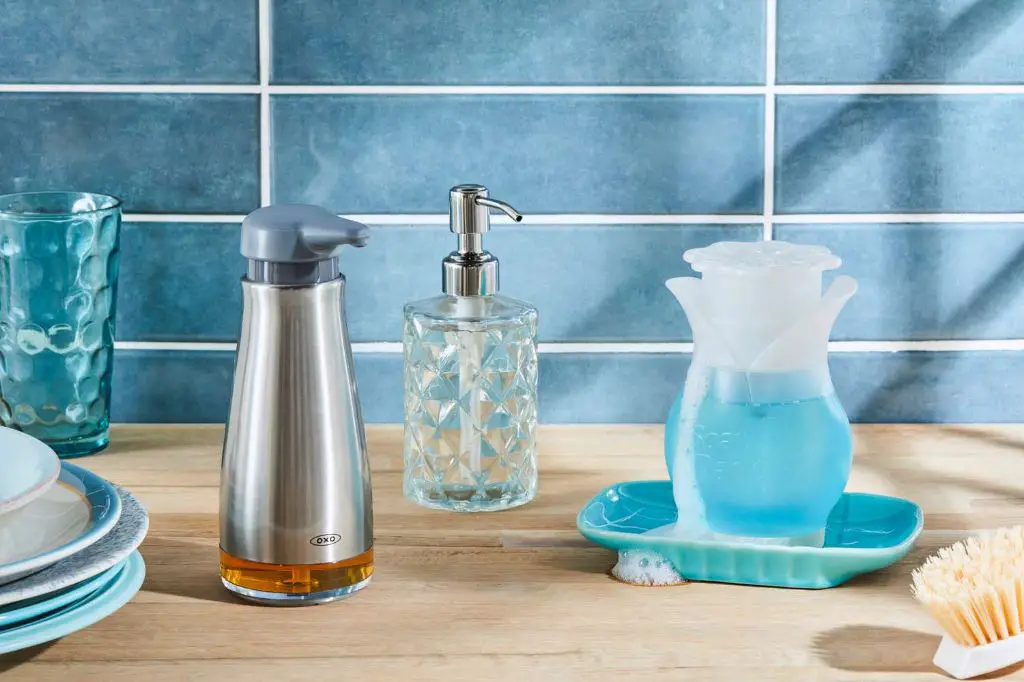 a person scrubbing a soap dispenser pump with a toothbrush