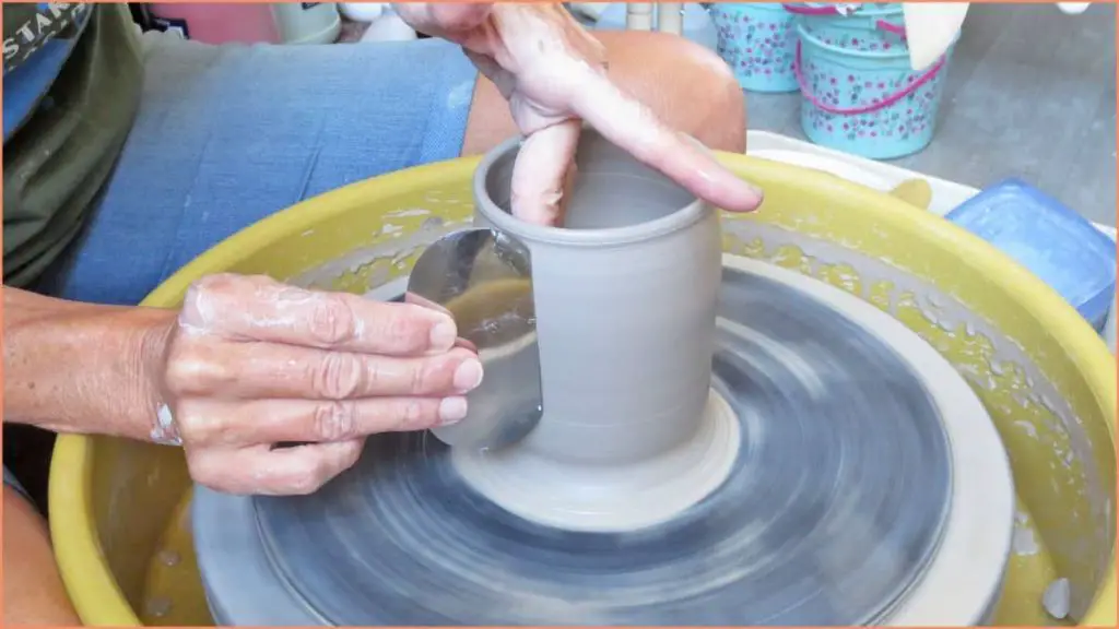 a person using a scraper tool to smooth and shape clay on a pottery wheel.