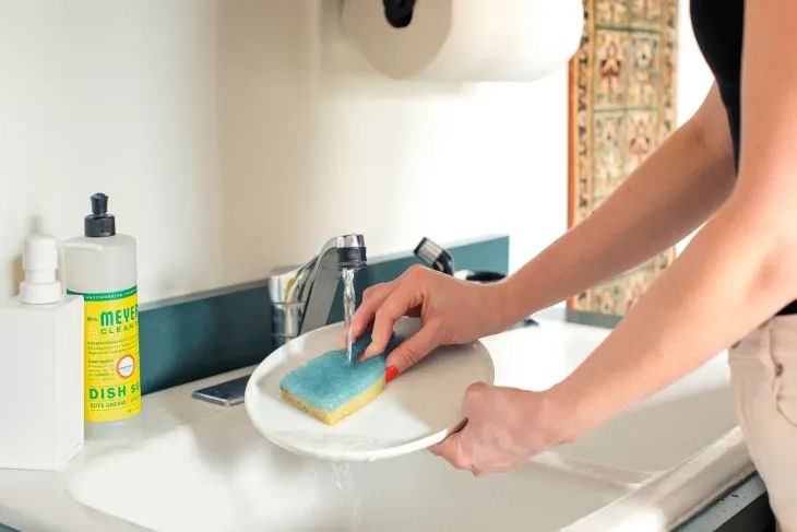 a person using a sponge to wash dishes in a kitchen sink filled with soapy water.