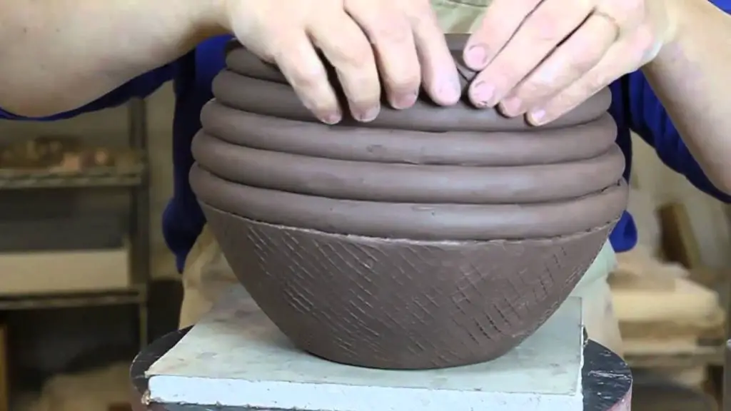 a person using clay coils to build a pottery vessel.