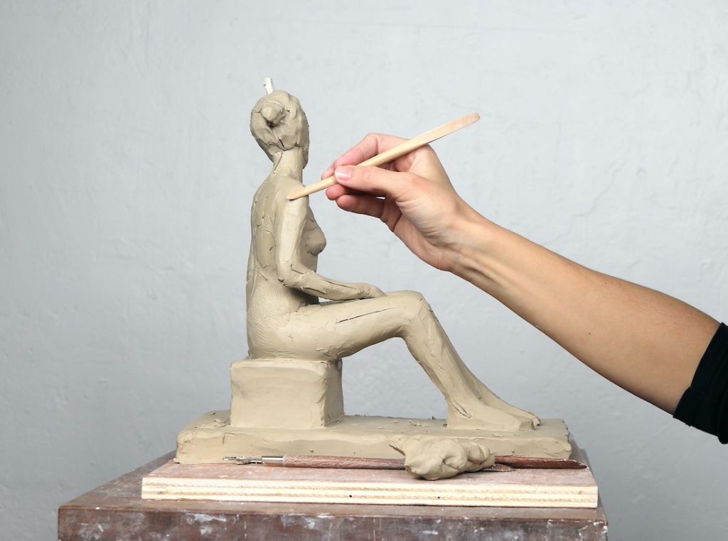 a person using clay sculpting tools to shape a small clay figure on a turntable.