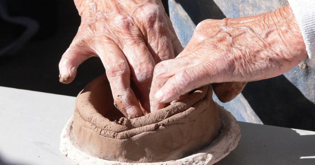 a person working on a clay pottery project, focused on keeping the clay moist.