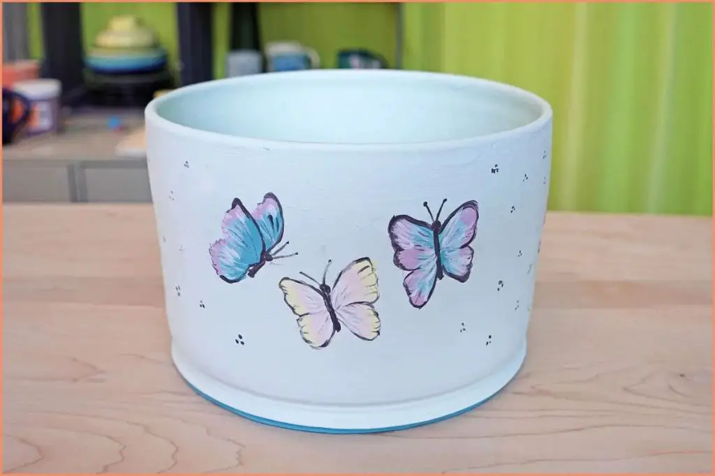 a potter applying colorful underglaze designs to a bisqueware vase before firing.