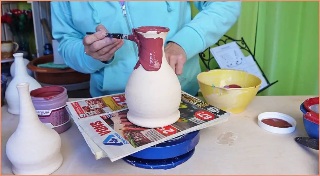 a potter brushing a raku glaze onto a ceramic piece