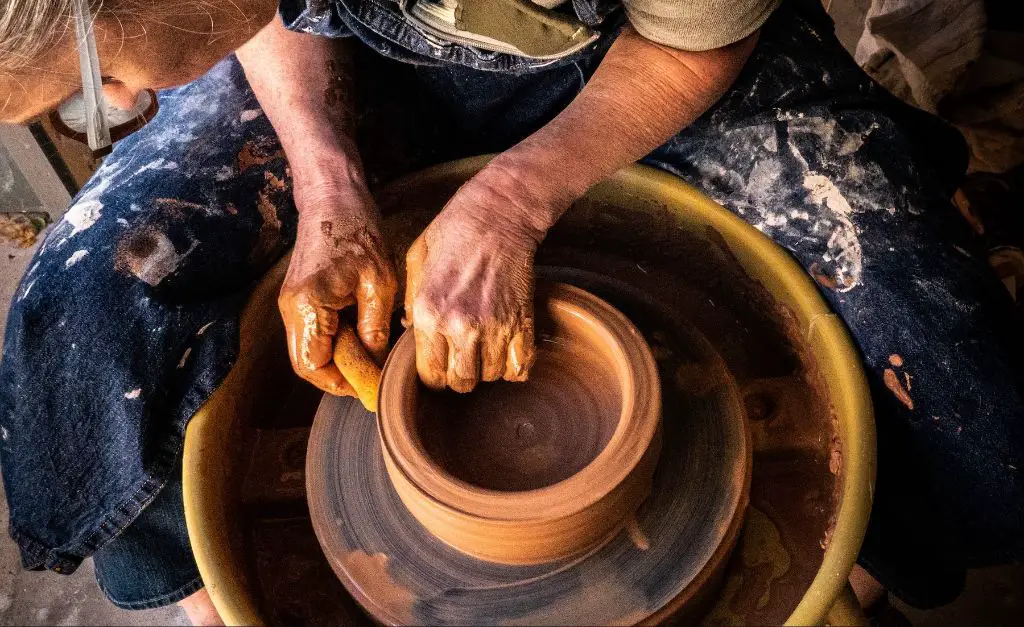 a potter using her hands to shape clay on a wheel.