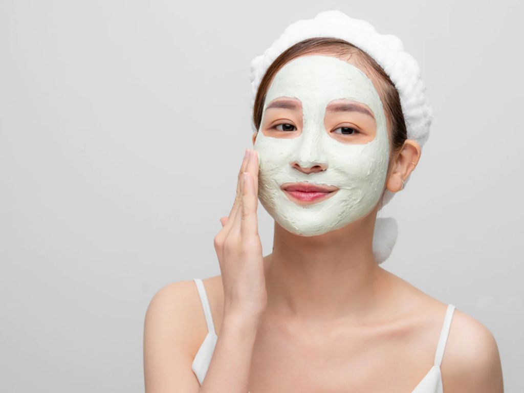 a woman applies a kaolin clay facial mask.