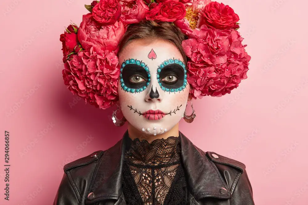 a woman with pink day of the dead face paint smiling happily