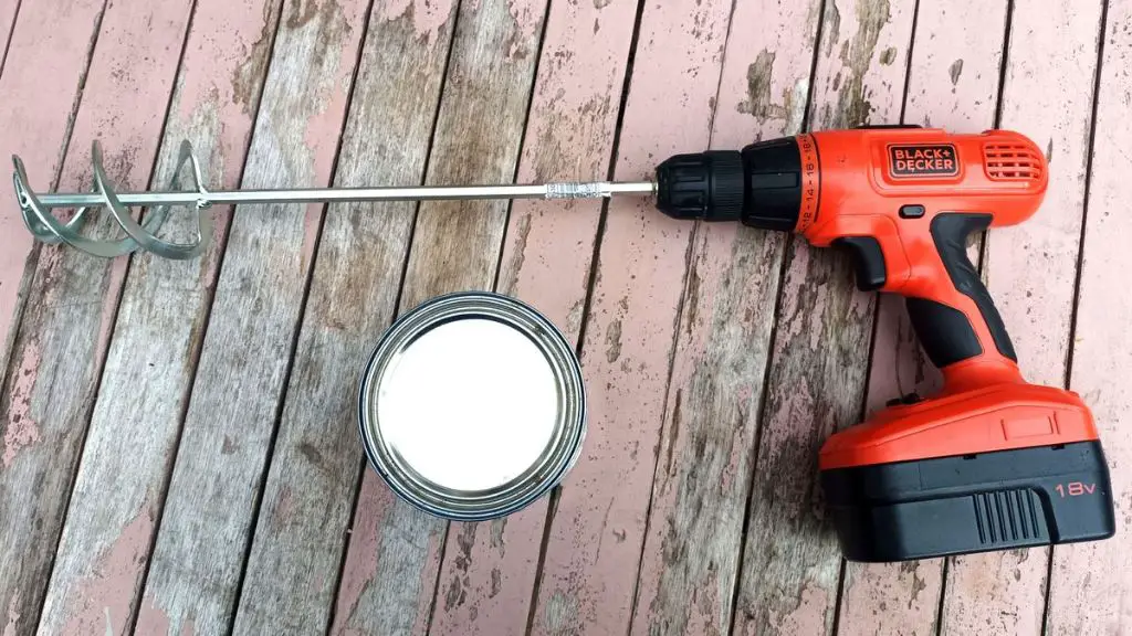 a worker using a cordless drill with mixing paddle to blend mortar.