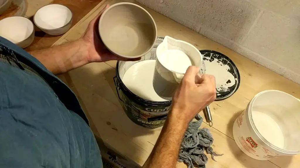 an artisan using a brush to carefully apply a shiny ceramic glaze to a handcrafted pottery bowl fresh from the kiln