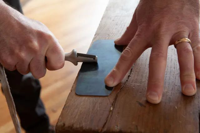 close up image showing the process of sharpening a hand scraper blade on a sharpening stone.