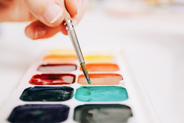 close up photo of watercolor paints in a palette with a paintbrush