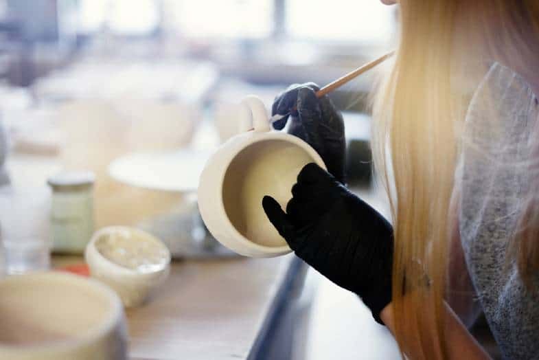 glaze being applied to an unfinished clay pot before firing in a kiln.