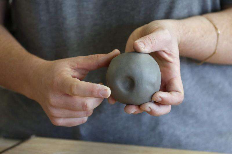 hands pinching and shaping a ball of clay into a pinch pot