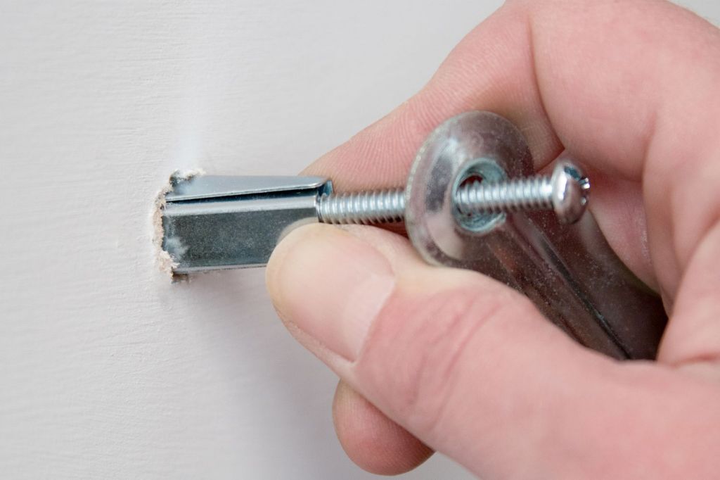 person installing a toggle anchor into a wall stud
