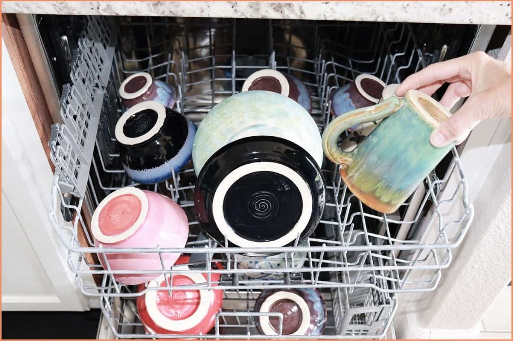 person loading handmade ceramic mugs into a dishwasher