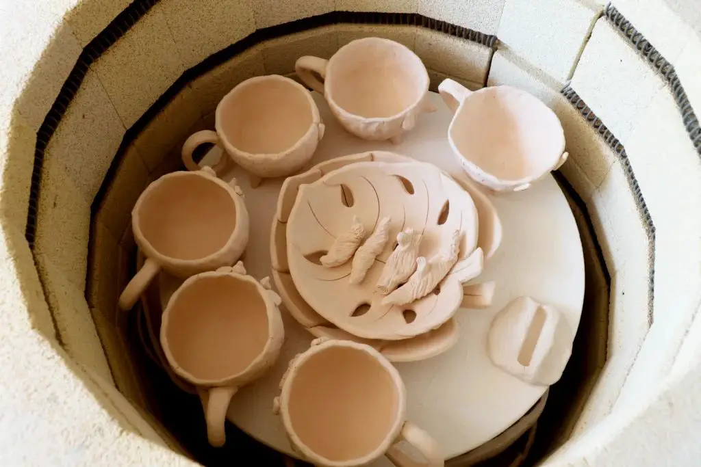 person loading porcelain pottery pieces into a ceramic kiln to be fired