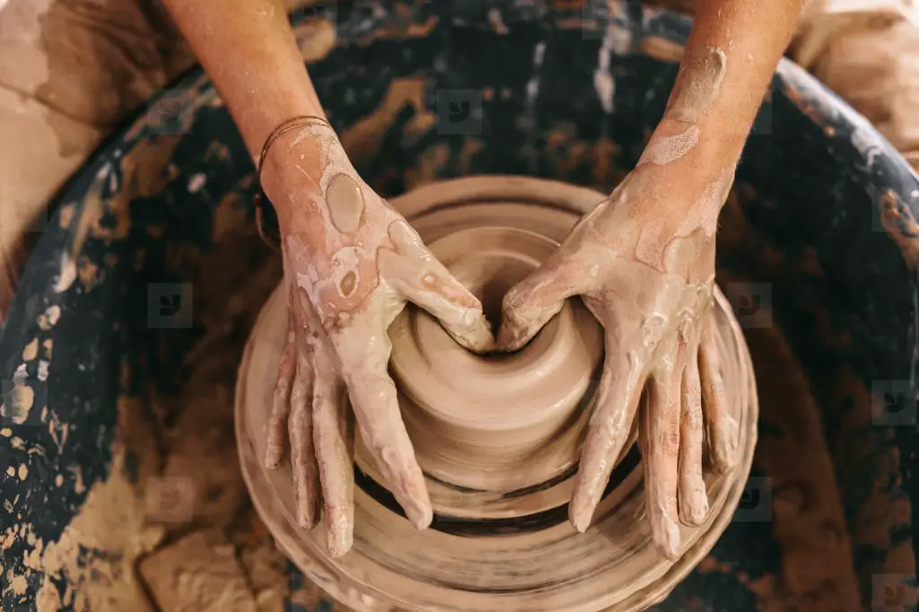 person molding clay pot on pottery wheel