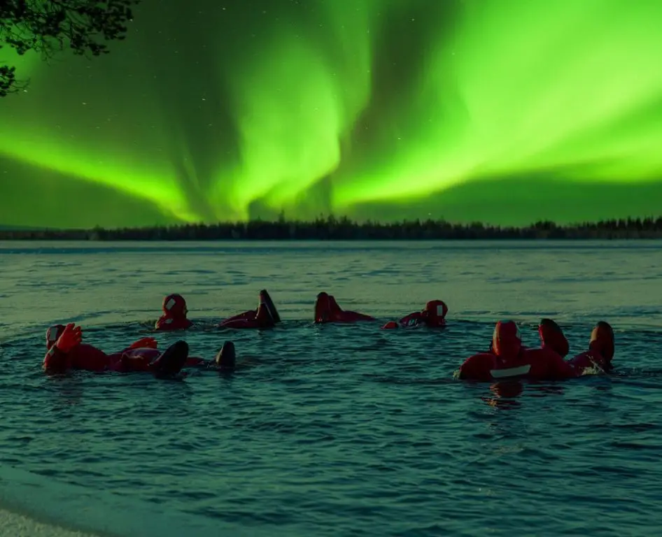 person photographing aurora borealis over a frozen lake