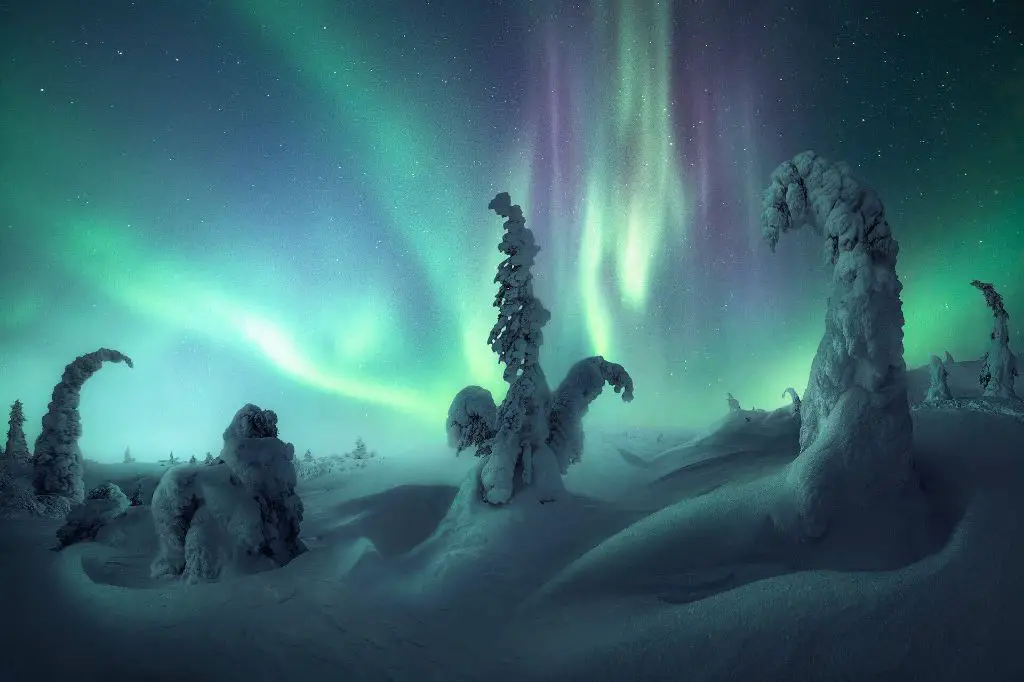 person photographing aurora borealis over a frozen landscape