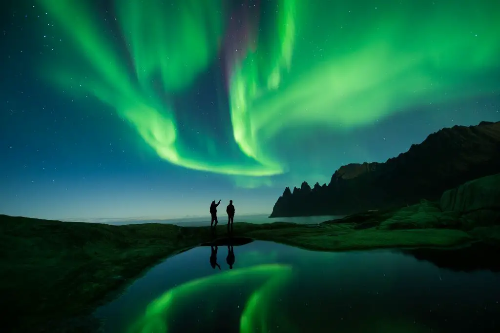 person photographing aurora borealis over a mountain landscape