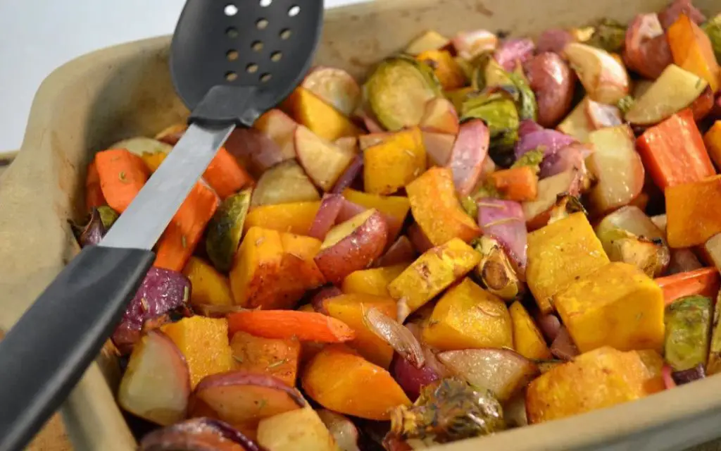 person removing a stoneware plate of roasted vegetables from the oven