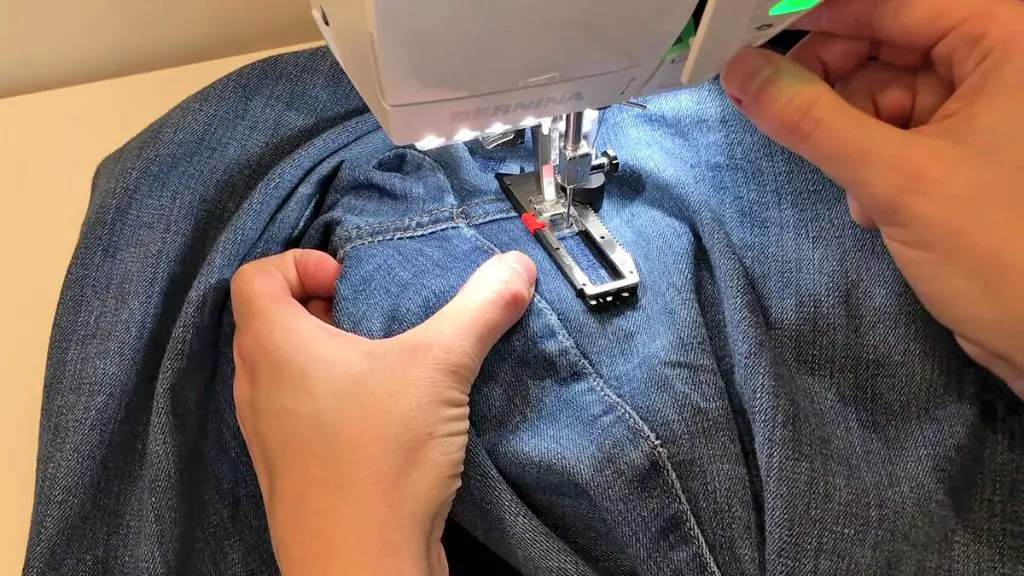 person sewing a patch over a hole in jeans