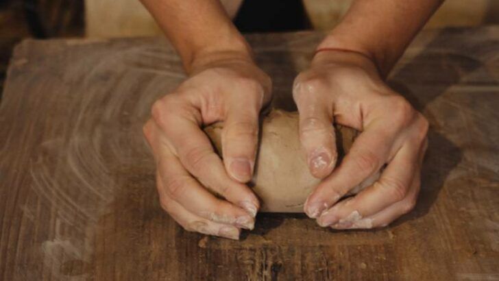 person wedging and kneading clay on a table to prepare it for pottery.