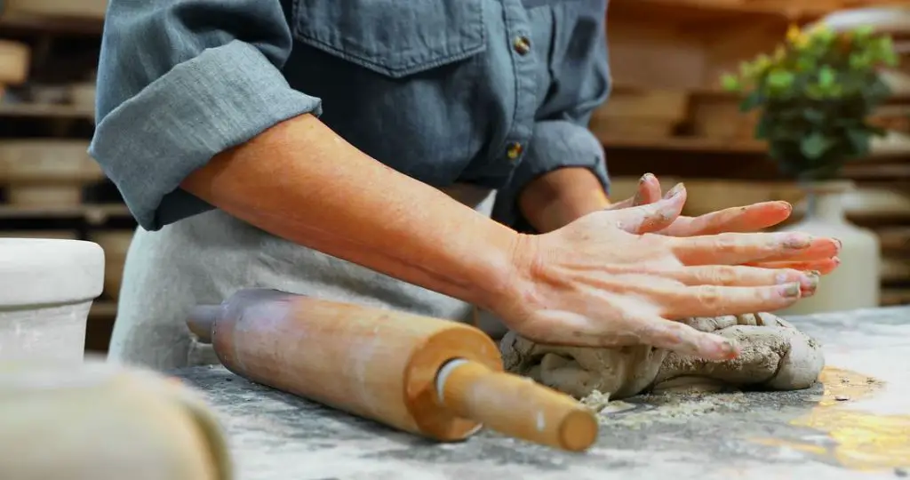 person's hands kneading baking clay dough on a floured surface.