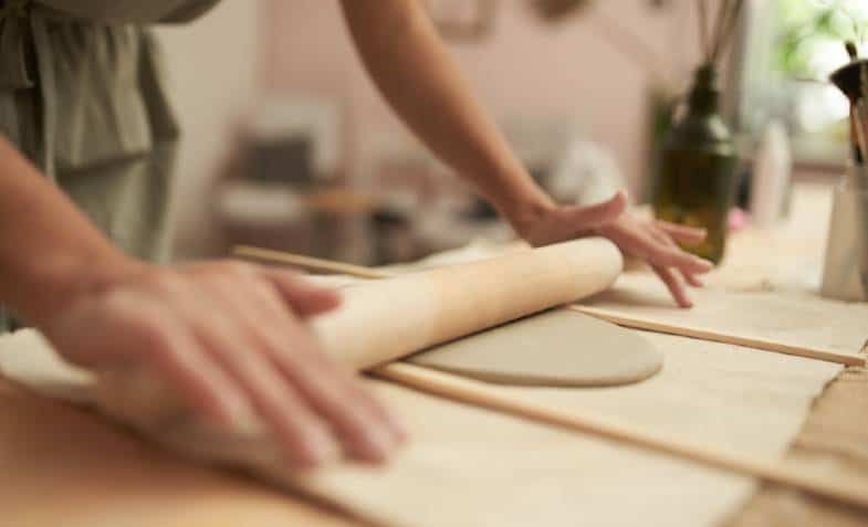 rolling out clay slabs by hand using a slab roller allows consistency and efficiency in handbuilding pottery and ceramic vessels.