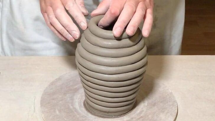 someone using the clay coiling technique to build up a rounded, curved ceramic sculpture by stacking and blending coils of clay.