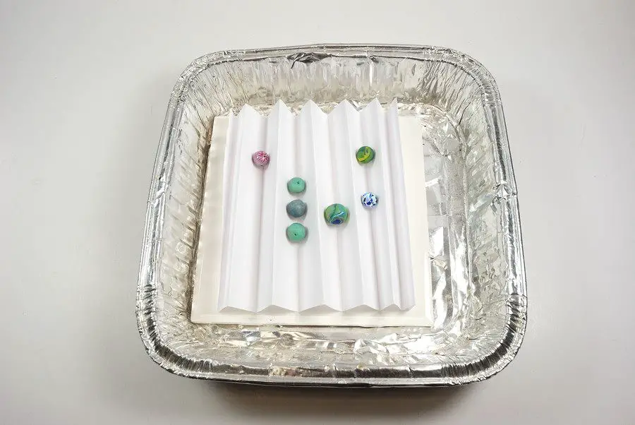 tray of thin polymer clay beads baking in an oven