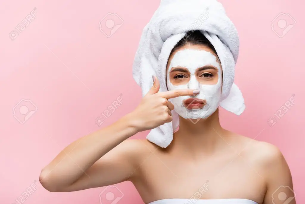 woman applying a clay mask to nose and forehead