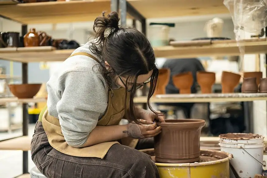 woman wearing patterned apron working with clay on pottery wheel