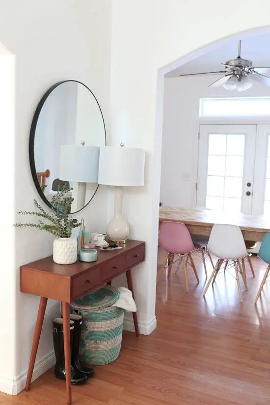 A big round mirror above table with a skinny lamp