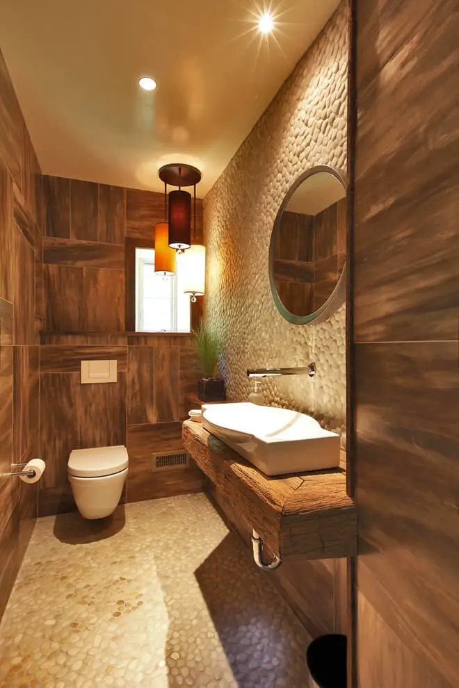 #10. Small rustic beige tile and pebble tile powder room with wood countertops, a wall-mount toilet, a trough sink and brown countertops